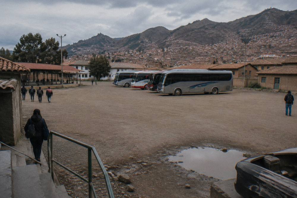 Buses parked at an open-air terminal in Cusco with hills behind them