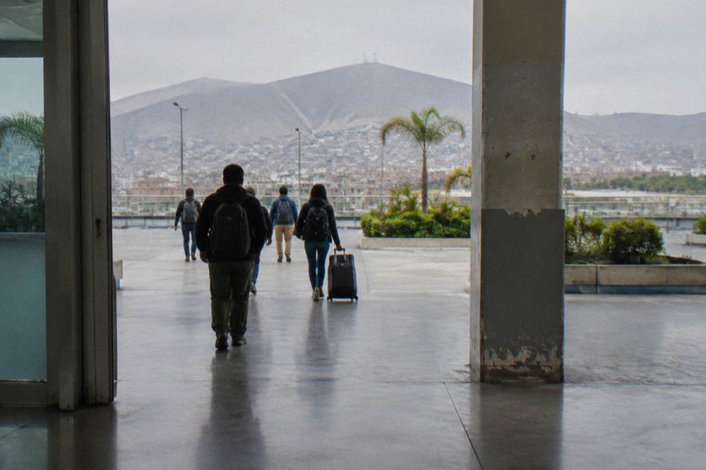 Travelers with backpacks waiting in a bright terminal hall beside a departure board