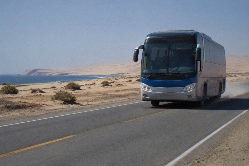 A highway coach travelling along a desert road with dunes on the horizon