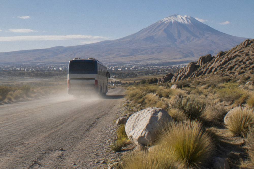 A passenger bus on a two-lane highway crossing a wide barren Andean plateau