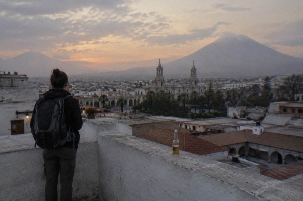 A traveler with a backpack looking out over the red rooftops of central Cusco toward the surrounding hills