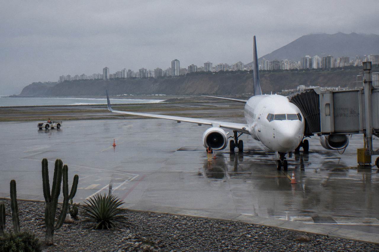 A commercial airplane parked at a gate at Jorge Chavez International Airport in Lima under an overcast coastal sky