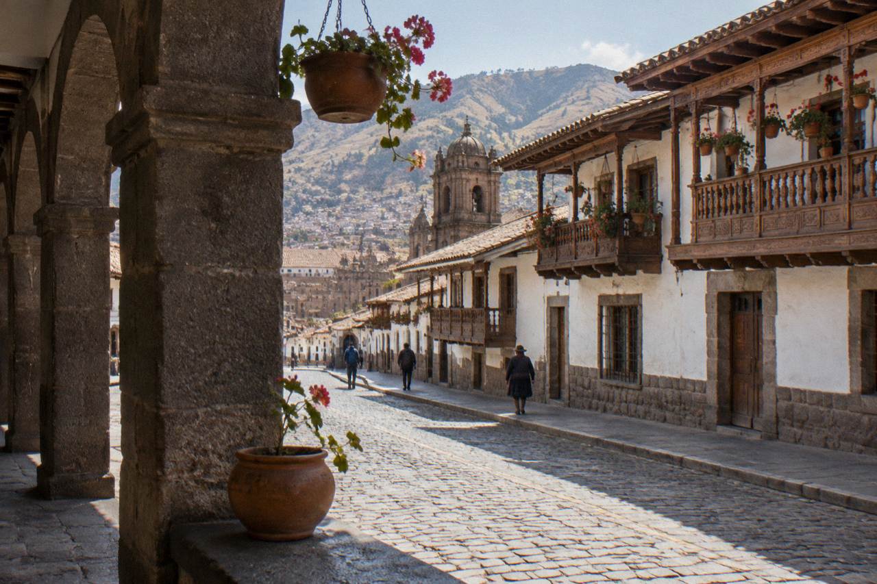 Sunlit colonial street with stone archways and hanging flower pots in Cusco's historic center