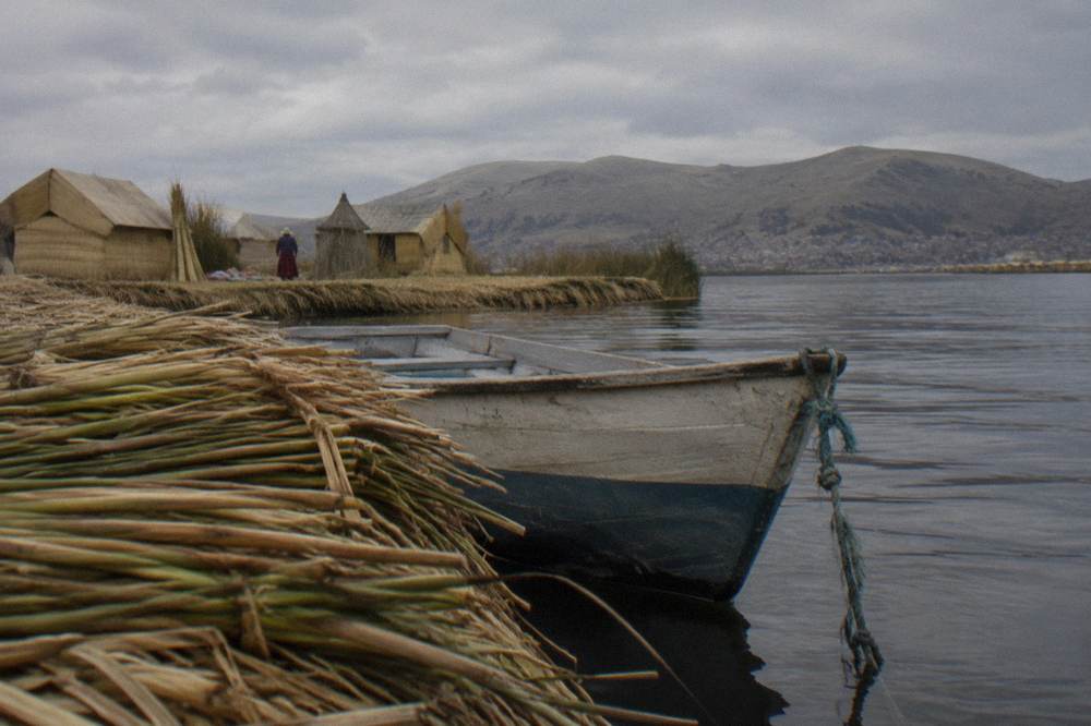 A small boat floating beside reed islands on a wide high-altitude lake with distant hills