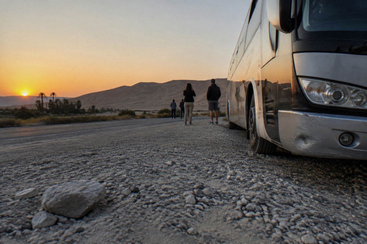 A long-distance tour bus parked on a desert highway with sand dunes in the background