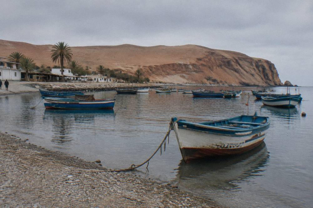 Small tour boats resting on calm water near a rocky shoreline at dawn