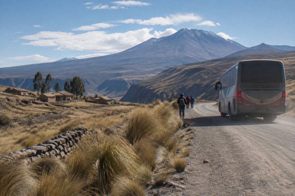 A long-distance bus traveling on a two-lane road through high open altiplano grassland under a wide sky