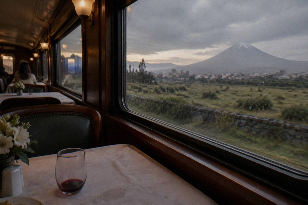 A vintage dining car interior with set tables and large windows facing open grassland