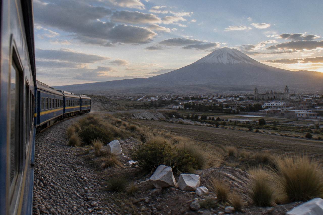 A blue and yellow train winding through open high-altitude grassland near Lake Titicaca