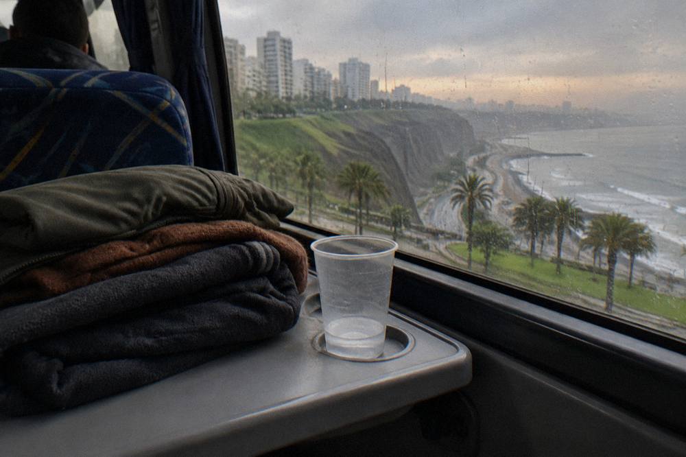 A folded stack of warm layers and a fleece jacket on a bus seat tray