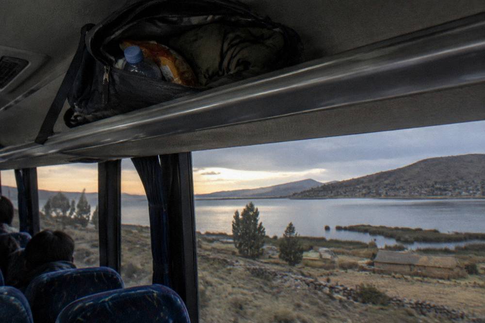 An open daypack on a bus luggage rack holding a water bottle, snacks and a jacket