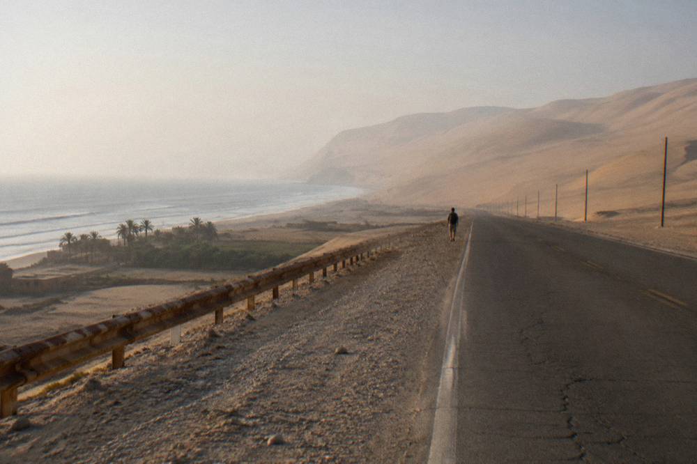 Open desert road along Peru's coast with sand dunes on one side and ocean haze beyond