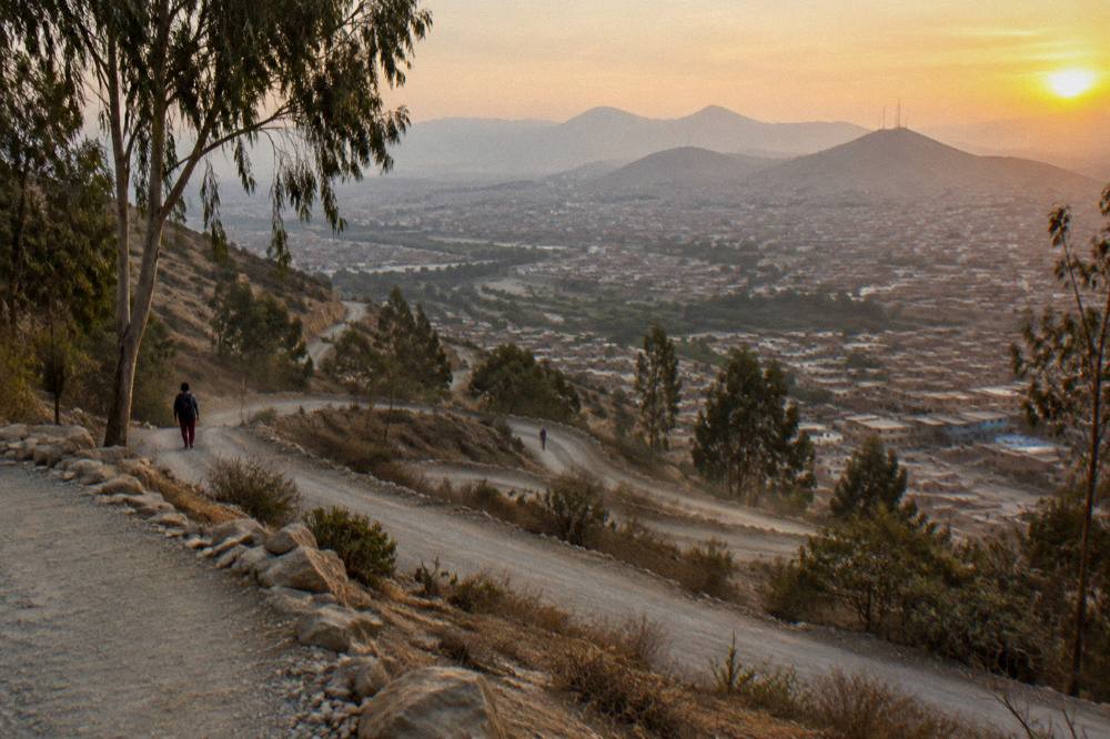 Mountain road with switchbacks descending toward a valley town at golden hour