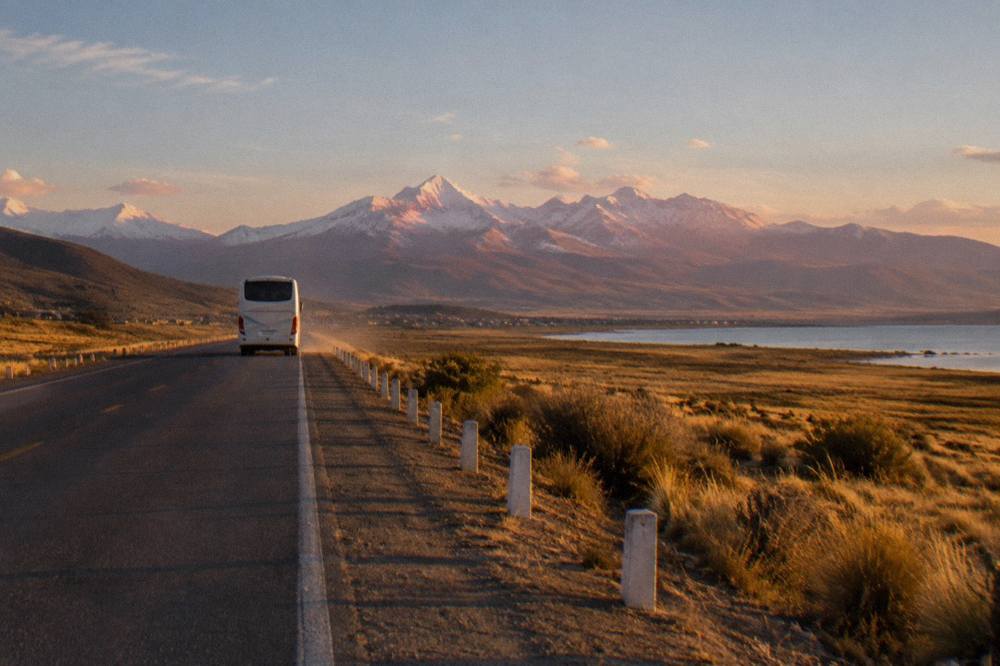 A touring bus travelling on a two-lane highway through open altiplano grassland with distant mountains