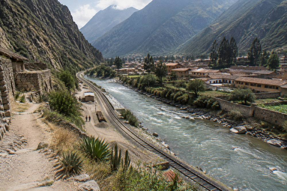 A mountain town beside a river with a rail line and forested peaks in mist