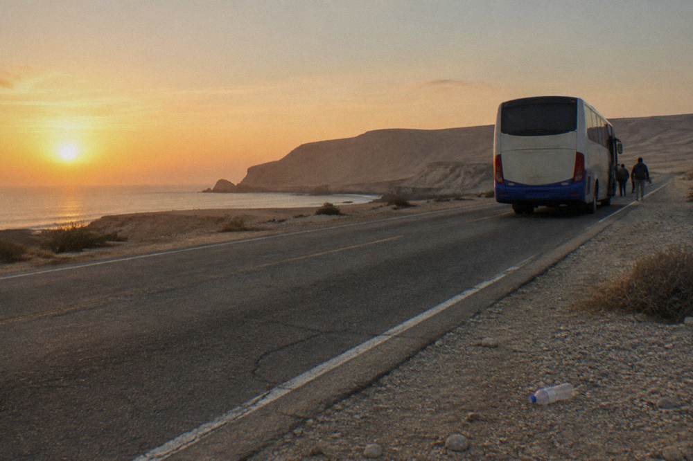 A long-distance bus traveling on a desert highway near the Peruvian coast