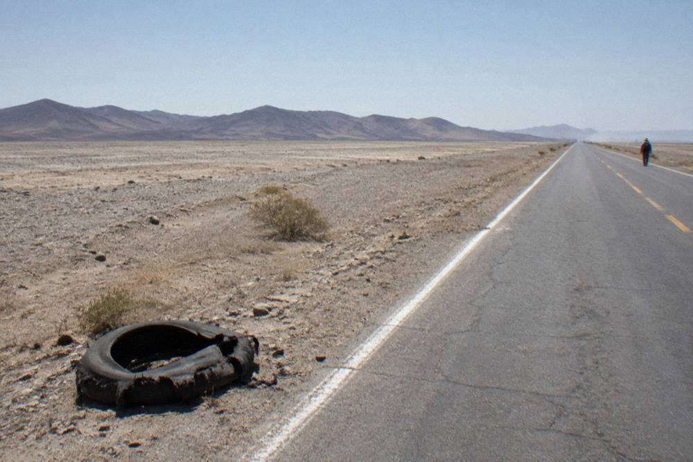 Straight desert highway crossing empty arid plains with low hills on the horizon
