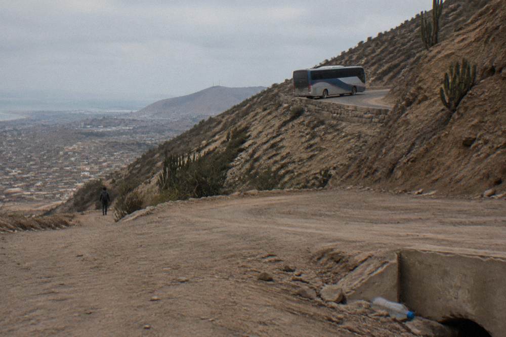 A long-distance coach climbing a switchback road through brown Andean mountains