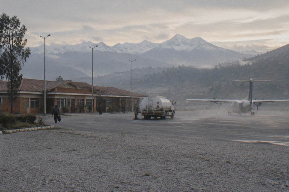 A small airport terminal building with mountains behind it under morning light