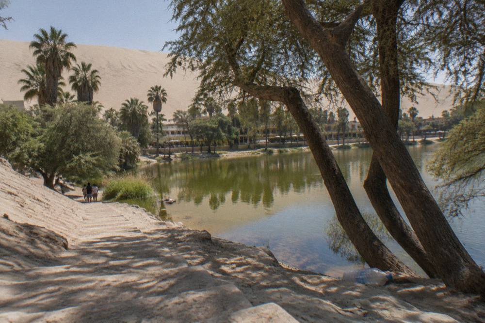 A desert oasis lagoon ringed by tall sand dunes under afternoon light