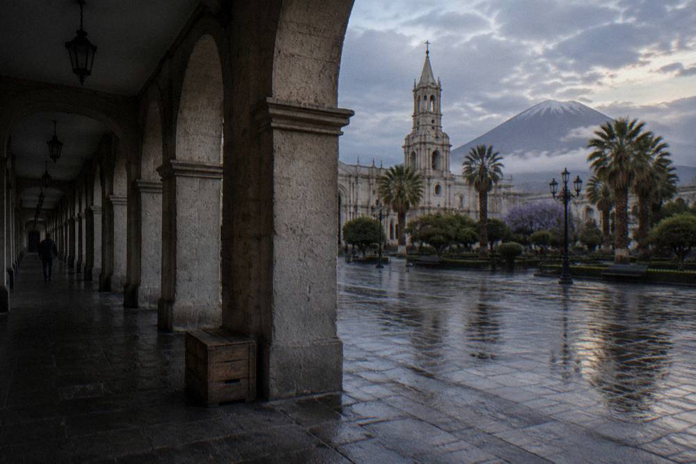 A colonial stone arcade of pale volcanic rock beside a quiet city plaza
