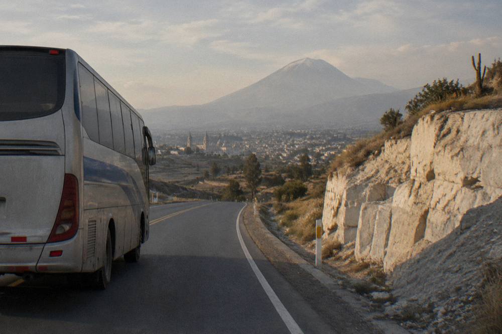 A touring bus driving along a two-lane highway through arid desert hills in southern Peru