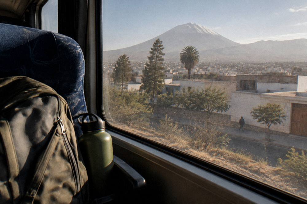 A traveler's daypack and water bottle resting on a bus seat beside a window with mountain views