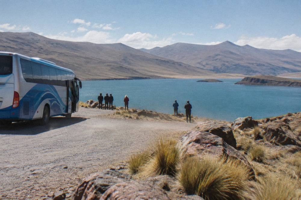 A tour bus parked beside a viewpoint overlooking a turquoise highland lake on the altiplano