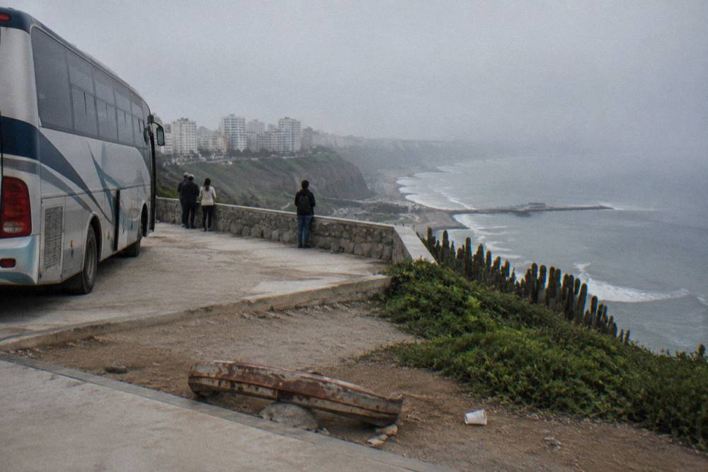 A touring bus parked beside a viewpoint overlooking an ocean bay at midday