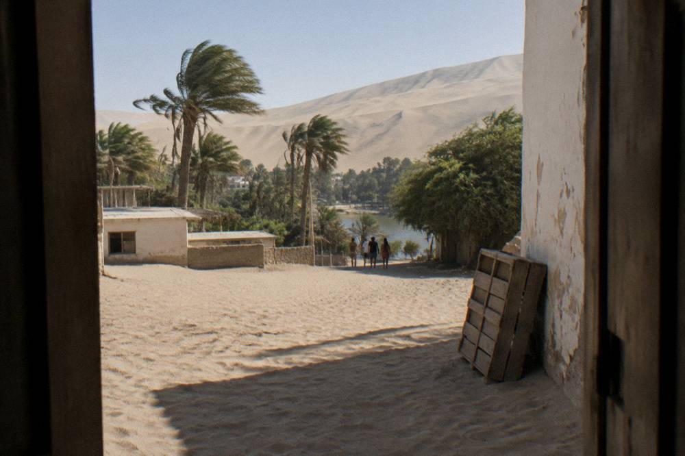 A small village street lined with low buildings at the base of towering sand dunes