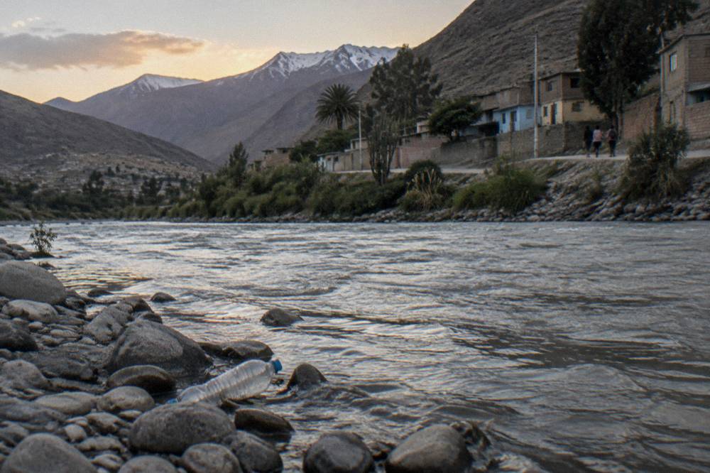 Narrow valley road beside a glacial river with jagged snow covered peaks rising above