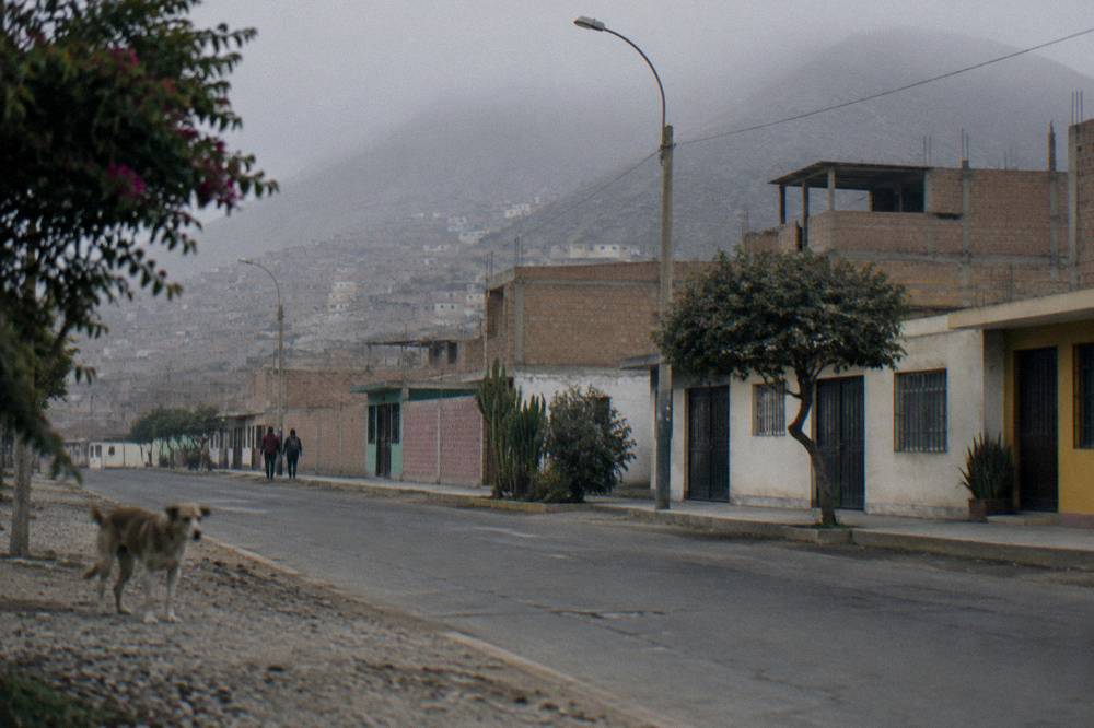 Town street in a high Andean valley with rocky peaks behind low buildings under clear sky
