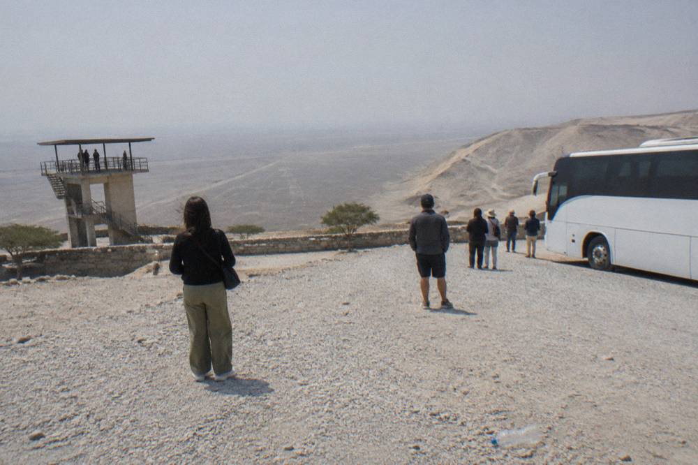 Modern tour bus parked at a desert stop with passengers waiting to board