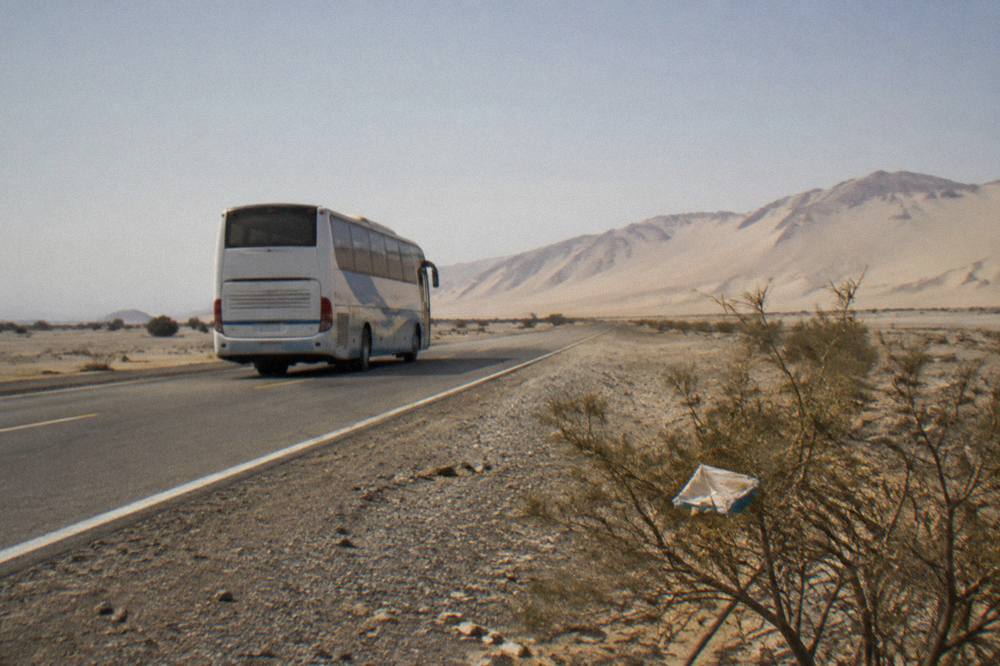 Tourist bus travelling on a desert highway along the Peruvian coast with sand dunes in the distance