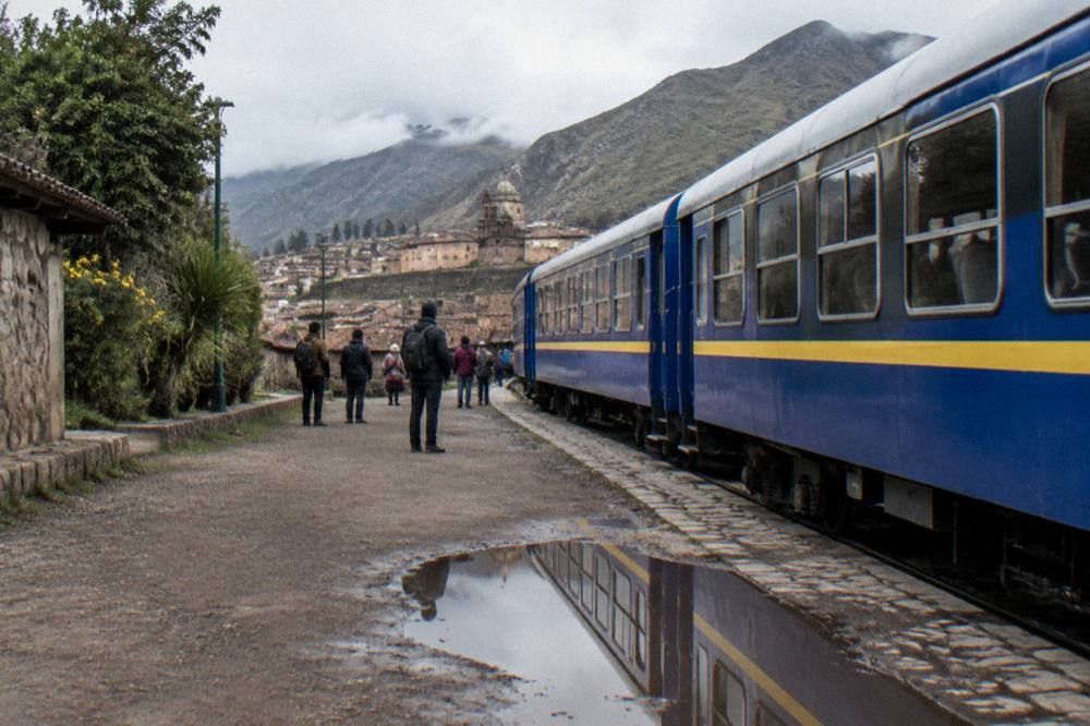 Blue and yellow excursion train stopped at a highland station with passengers on the platform