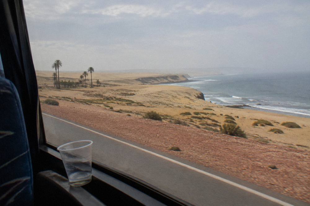 View from a bus window of desert dunes along the coastal highway with the Pacific Ocean beyond