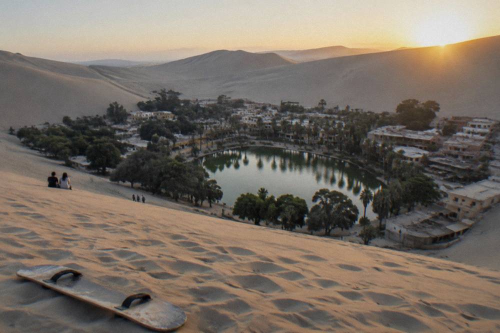 Oasis lagoon ringed by palm trees and tall sand dunes at Huacachina
