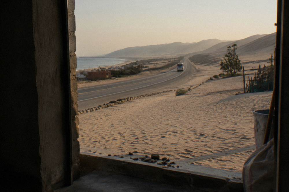 A desert highway stretching south past sand dunes toward distant mountains at golden hour