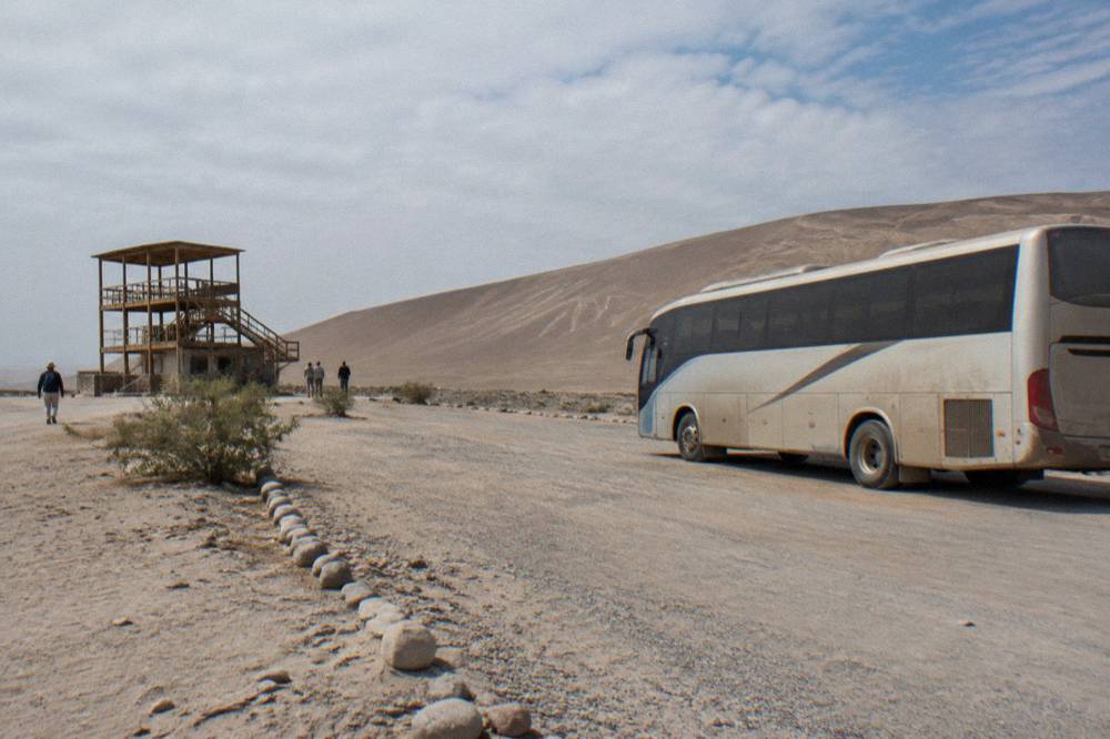 Tourist bus parked beside a desert road with dunes rising behind it