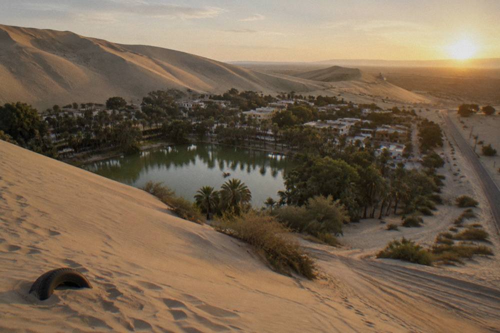 Aerial view of an oasis town ringed by sand dunes beside a desert highway