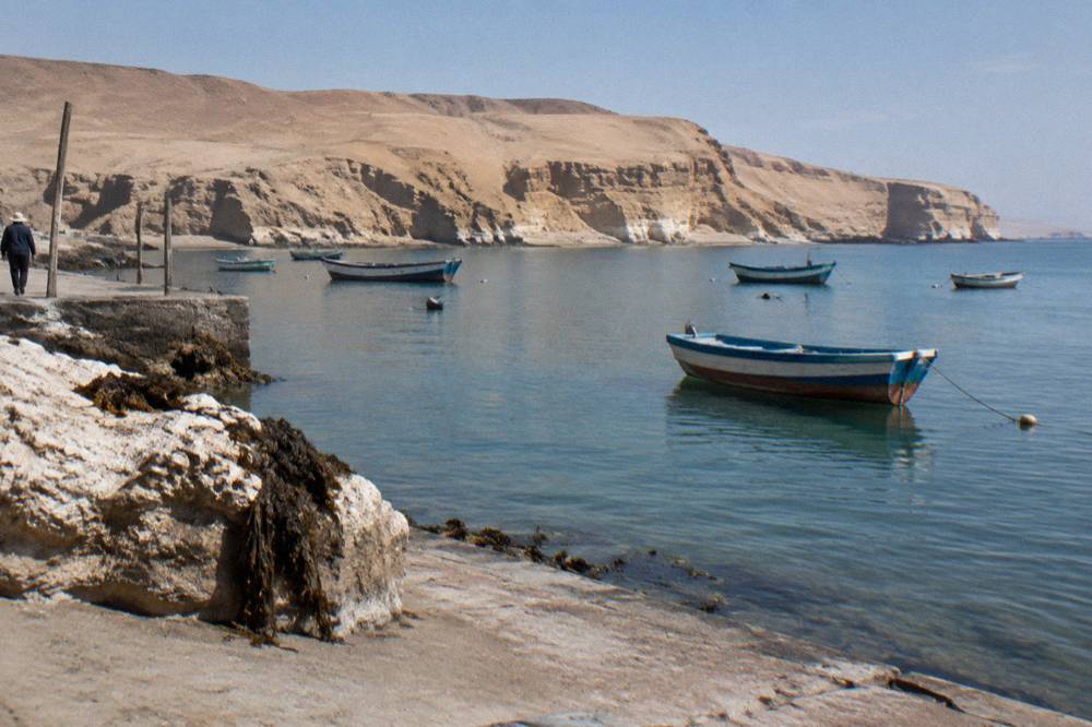 Cliff-lined bay with small boats and arid hills under morning light