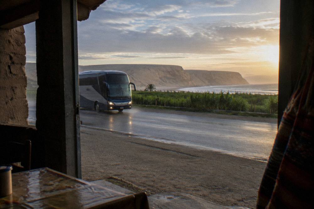 A touring bus driving along a coastal highway with ocean cliffs in the background