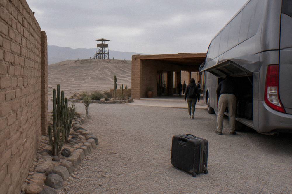 A touring bus parked outside a hotel entrance while luggage is loaded into the hold