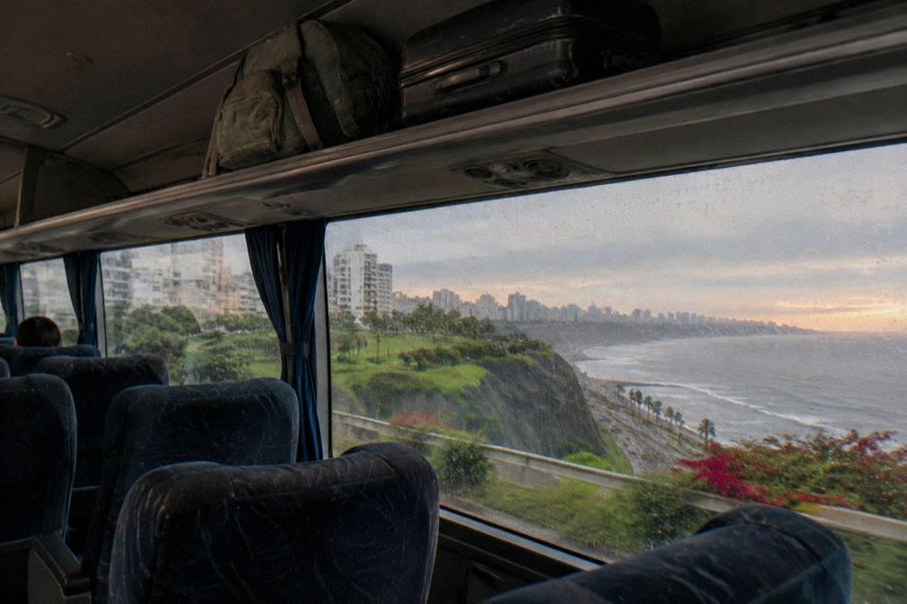 A traveler's daypack and suitcase resting in an overhead rack inside a bus cabin