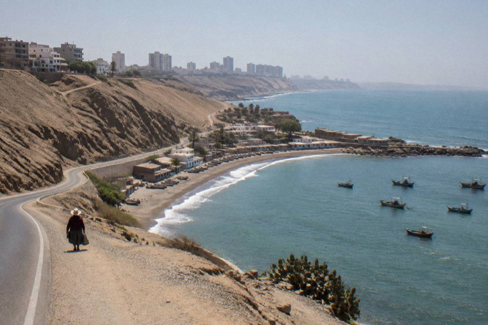 A coastal desert road curving beside cliffs with a small fishing bay below