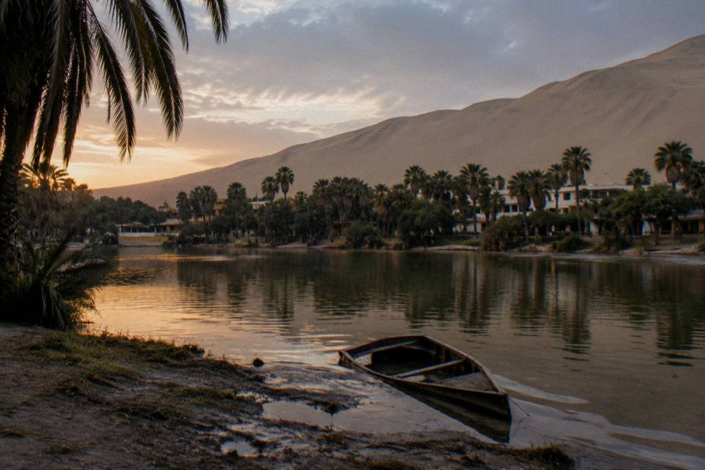 An oasis village with a lagoon surrounded by palm trees and steep sand dunes
