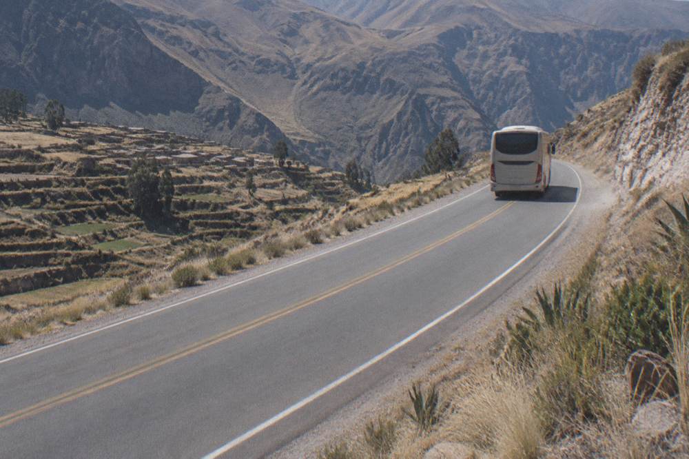 A long-distance tour bus traveling on a two-lane highway through open highland terrain