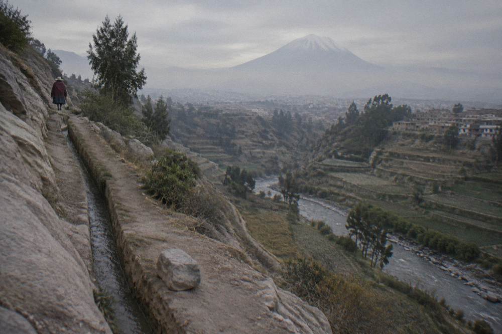 A deep canyon with terraced farmland on its slopes and a river winding along the valley floor