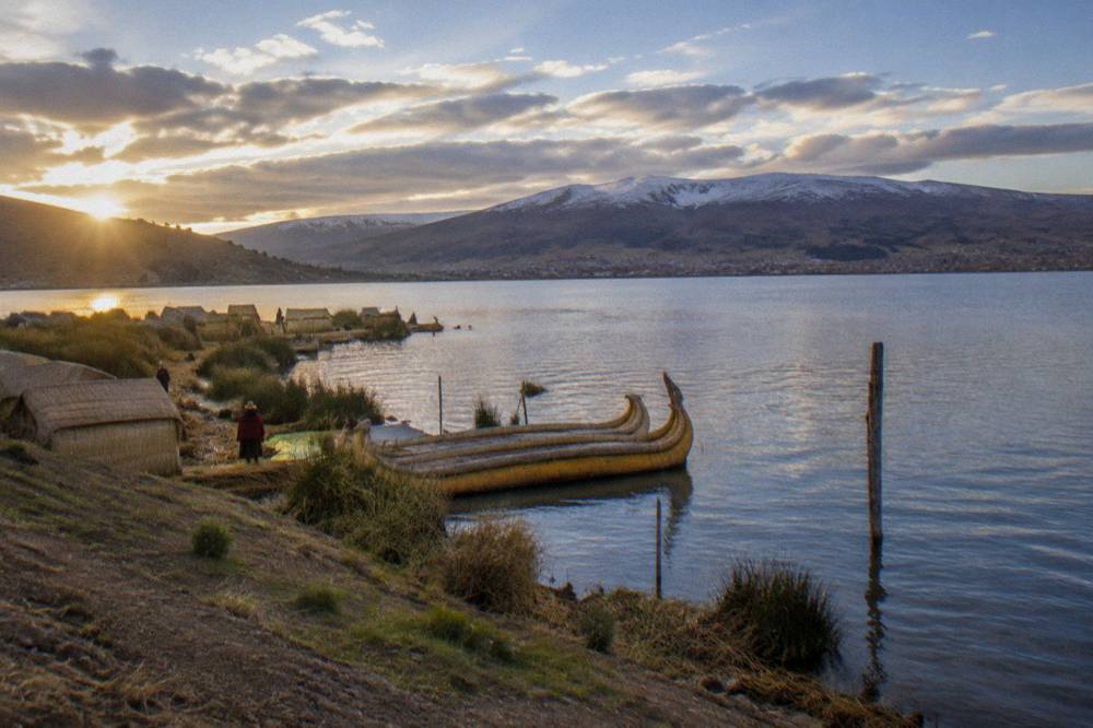 A wide high altitude lake with reed boats and distant snow dusted hills under a bright sky