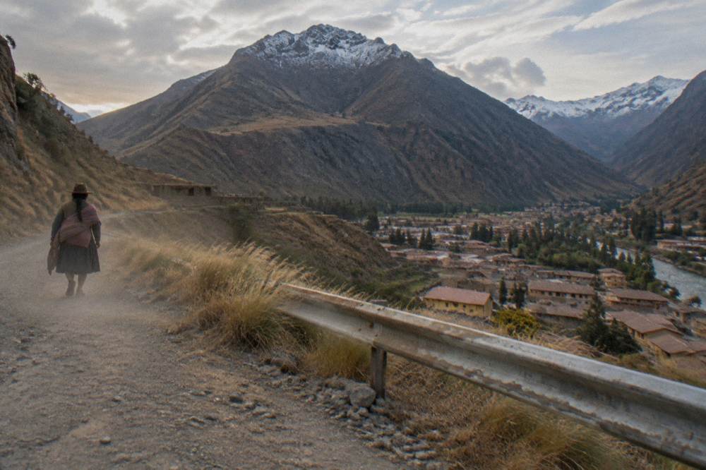 A high mountain pass sign on a windswept altiplano road with snow-dusted peaks behind it